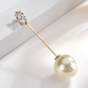 Macro detail of a gold-plated brooch pin featuring a marquise gemstone and white pearl