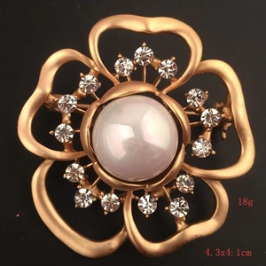 Detail of matte gold camellia brooch with large pearl center and sparkling rhinestones