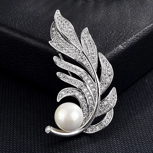 Gros plan sur une broche plume argentée avec pavé de zircons et perle blanche