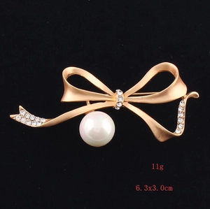 Detail view of a gold bow brooch with a large white pearl and sparkling rhinestones
