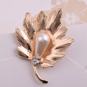 Gros plan d'une broche feuille dorée avec texture nervurée, perle goutte et cristaux brillants
