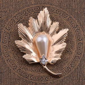 Détail de la broche en feuille d'érable dorée avec perle en goutte et strass scintillants