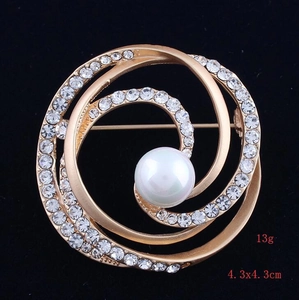 Detail of matte gold spiral brooch with white rhinestones and a central pearl