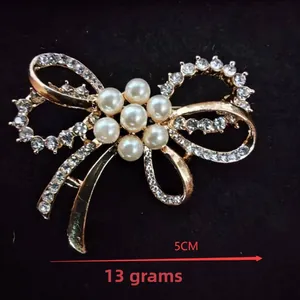 Close-up of golden bow brooch with small white rhinestones and centered pearl flower