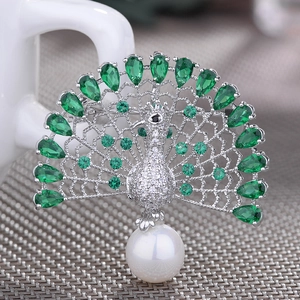 Elegant peacock brooch with green zircons and a white pearl on a silver textured base