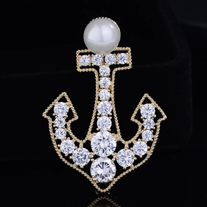 Detailed close-up of a gold anchor brooch with white pearl and sparkling crystals