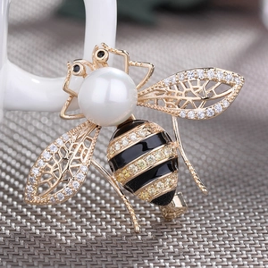 Eleganter Goldbienen-Brosche mit großer weißer Perle und Zirkonia-Flügeln auf grauem Stoff
