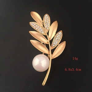 Detail view of a matte gold leaf brooch with micro-pave crystals and a large white pearl