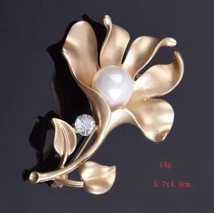 Detail view of matte gold flower brooch with white pearl center and clear rhinestone
