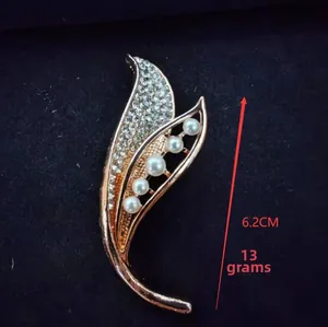 Close-up of leaf-shaped brooch with white pearls and rhinestones on blue velvet