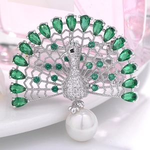 Macro shot of silver peacock brooch with emerald crystals and a hanging white pearl