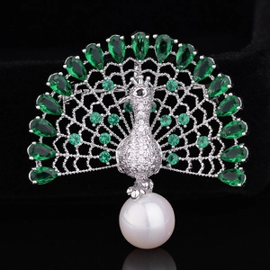Detail of peacock brooch with green zircons and a large white pearl on black background