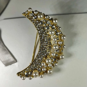 Vue détaillée d'une broche croissant dorée ornée de cristaux et de perles blanches