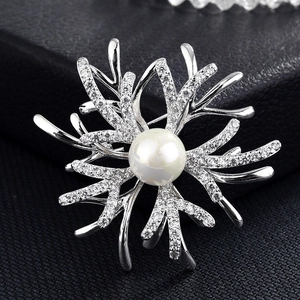 Détail macro d'une broche corail argentée avec zircons brillants et une grande perle blanche