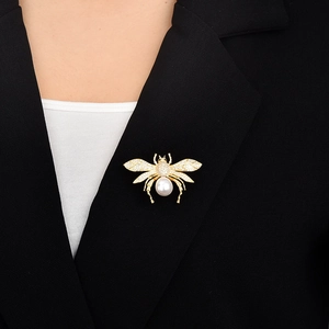 Detaillierte Nahaufnahme einer goldenen Bienenbrosche mit weißen Perlen und Zirkonia auf Blazer
