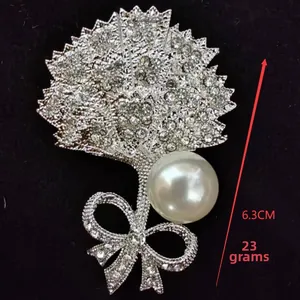 Detailed view of fan-shaped rhinestone brooch with white pearl and bowknot charm, 6.3cm tall