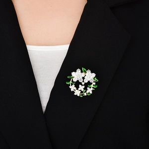 Dettaglio di una spilla a ghirlanda verde in zircone con foglie dorate su un blazer nero