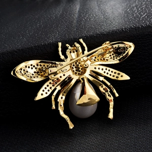 Goldene Insektenbrosche mit grauer Perle und Wabenflügeln auf schwarzem Lederhintergrund