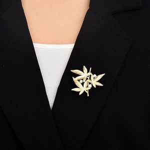 Detail of matte gold bamboo leaf brooch with pearls pinned on a black blazer jacket