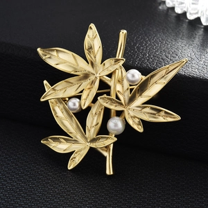 Elegant matte gold bamboo leaf brooch with three white pearls on black leather background