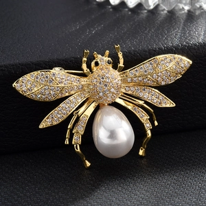 Detailaufnahme einer goldener Bienenbrosche mit Zirkonflügeln und Perle auf schwarzer Oberfläche