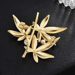 Elegant matte gold bamboo leaf brooch with white pearl on black leather background