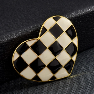 Gros plan d'une broche en forme de cœur avec émail à damier noir et blanc et bord doré