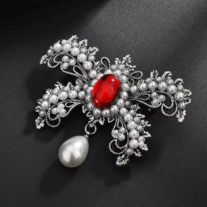 Détail macro d'une broche baroque avec gemme rouge, feuilles argentées et perle pendante