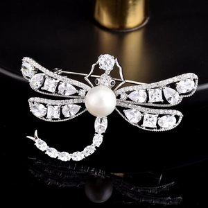 Détail macro d'une broche libellule avec micro-serti de zircons et une perle blanche centrale