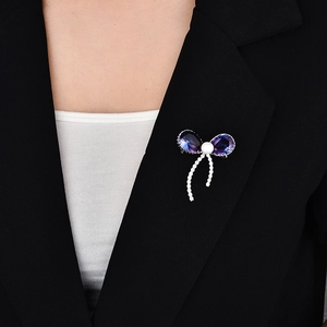 Détail d'une broche nœud en cristal violet avec perle et glands sur un blazer noir chic