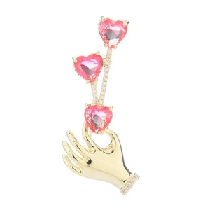 Detail of a golden hand-shaped brooch with pink heart gems and sparkling zircon accents