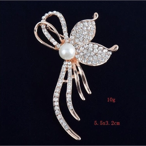Macro d'une broche fleur en or rose avec strass pavés et une perle blanche centrale