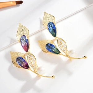 Detail of two leaf-shaped brooches with blue gradient stones and white pearls on gold alloy