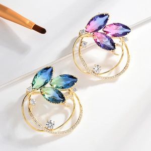 Detailed macro view of two marquise-cut gradient crystal floral brooches on a white background