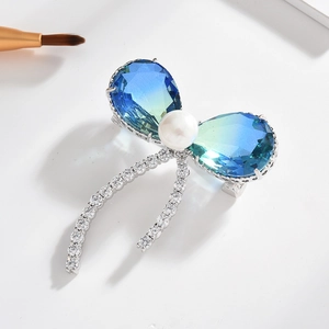 Broche papillon élégante avec cristaux bleu-vert, perle blanche et rubans sertis de zircons
