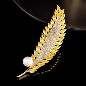 Détail macro d'une broche feuille avec pierres jaunes et perle blanche sur fond noir poli