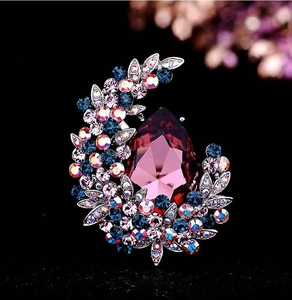 Macro shot of luxury brooch with large pear-cut purple gem and crystal-encrusted leaves