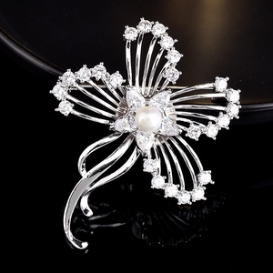 Gros plan d'une broche fleur en argent avec zircons et une perle blanche au centre