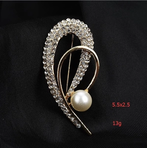Détail de la broche perle et strass avec dimensions 5,5x2,5 cm sur tissu noir élégant