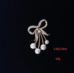Détail de la broche nœud dorée avec strass scintillants et perles blanches élégantes