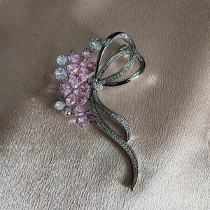 Elegant silver bow brooch with pink zircon flower petals on soft silk fabric texture