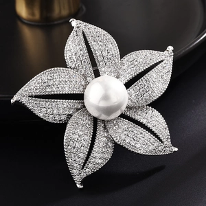 Elegant floral brooch with shimmering zircons and central pearl on a black surface