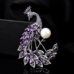 Détail de la broche paon avec pierres violettes et une grande perle blanche sur noir
