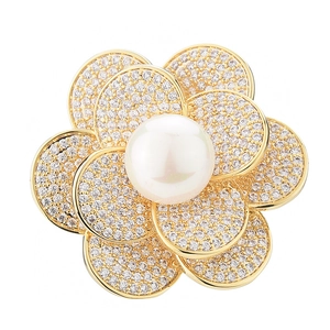 Elegant gold flower brooch with large pearl center and sparkling crystal petals on white background