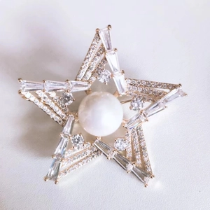 Macro detail of star brooch featuring a large pearl and sparkling zircon stones on gold base