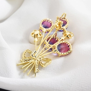 Élégante broche fleur dorée avec cristaux violets dégradés, perles et détail de nœud