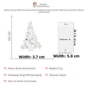 Size comparison of silver Christmas tree brooch with zircon and pearl against a phone