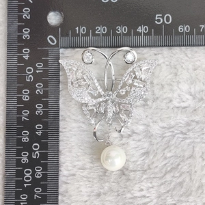 Vue détaillée d'une broche papillon argentée avec incrustation de zircone et pendentif perle