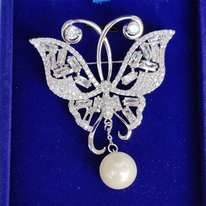 Élégante broche papillon en zircons avec perle blanche sur fond de velours bleu