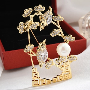 Macro detail of a golden brooch featuring birds on a branch with crystal and pearl